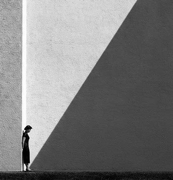 A lone person stands in a stark, geometric shadow.