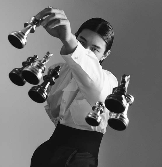 Person holding multiple Oscar trophies in black and white photo.