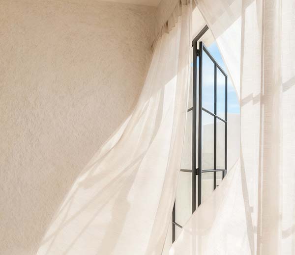 Sunlight filters through a softly billowing white curtain by an open window.