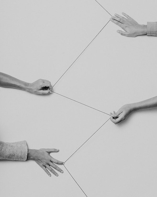 Three hands holding and pulling a string in different directions.