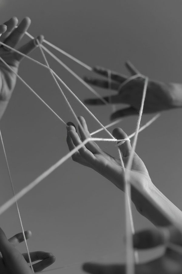 Hands intertwined with strings in an abstract black and white composition.